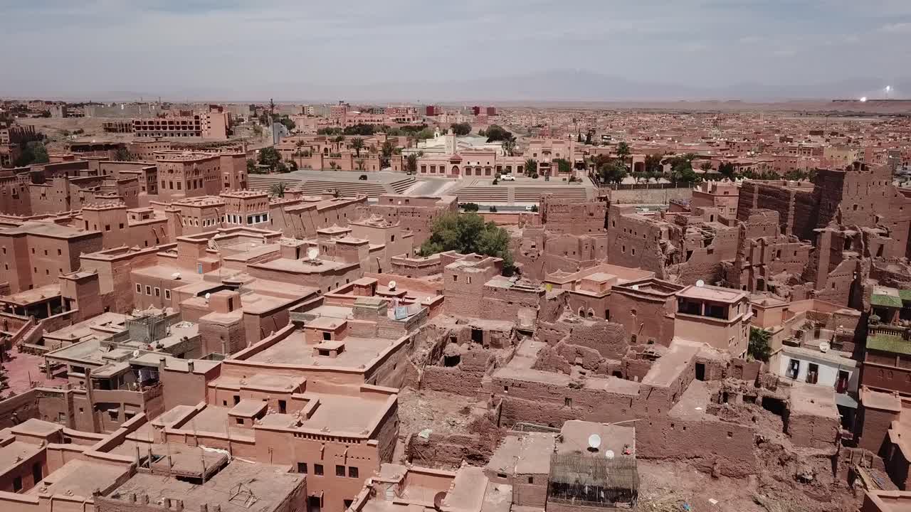 Ripresa cinematografica con drone che domina i tetti e gli edifici in terra battuta simili a un labirinto di un tradizionale Ksar marocchino a Ouarzazate, che si estende verso l'orizzonte del deserto arido.