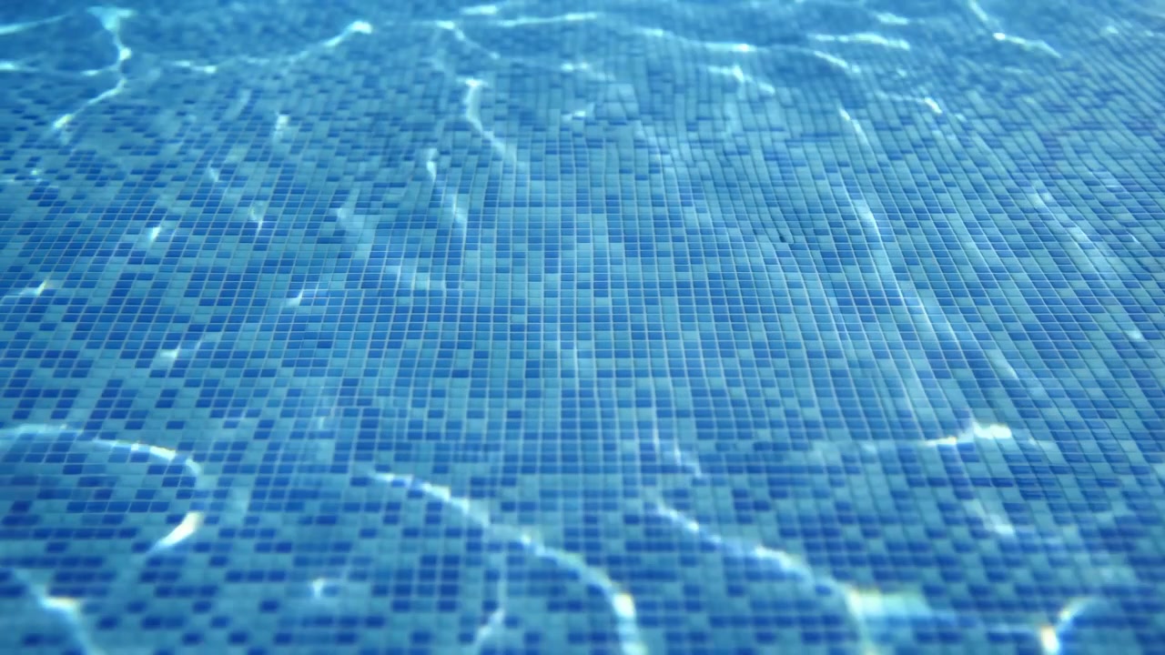 Ruhiges blaues Poolwasser kräuselt sich über eine geflieste Mosaikoberfläche, erzeugt schimmernde Sonnenlichtreflexionen und einen ruhigen Sommerhintergrund mit abstrakter Textur