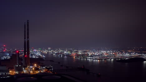 La-Central-Eléctrica-De-Poolbeg-Acumula-Luces-Parpadeantes-Con-Grúas-Del-Puerto-De-Dublín-Y-Luces-De-La-Ciudad-Por-La-Noche