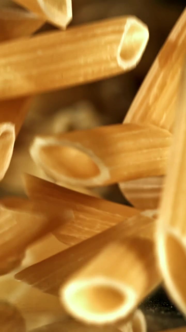 Pasta penne cruda che cade al rallentatore su una superficie riflettente