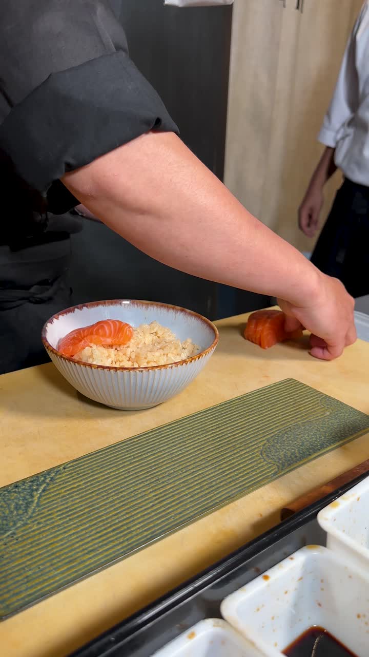Uno chef esperto usa le pinzette per disporre meticolosamente fette di salmone crudo su una ciotola di riso