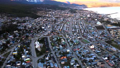 Drohnenaufnahme,-Die-über-Ushuaia,-Argentinien,-Fliegt-Und-Dabei-Nach-Oben-Schwenkt,-Um-Die-Vom-Sonnenuntergang-Beleuchteten-Anden-Zu-Zeigen