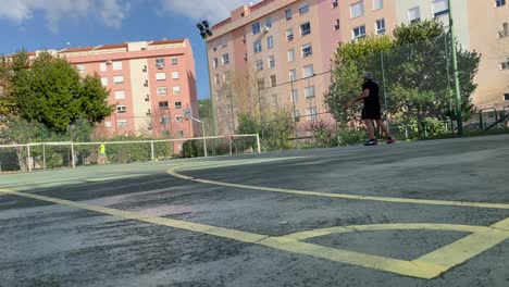 portrait of fit caucasian man serving with tennis racket on tennis court in sunny day in middle of residencial area in europe