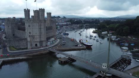 Ancient-Caernarfon-castle-Welsh-harbour-town-aerial-view-medieval-waterfront-landmark-close-orbit-left