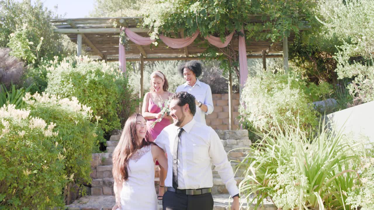 Después de la ceremonia, la novia y el novio tomados del brazo, descendiendo los escalones de la pérgola hacia la cámara con el ramo.