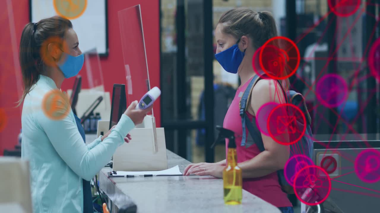 animación de iconos de los medios sobre una trabajadora caucásica con máscara facial tomando la temperatura