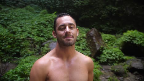 a young, attractive man with a happy and joyful facial expression taking his tongue out in a silly, playful way, looking into the camera and around his surroundings in the lush, green jungle of bali