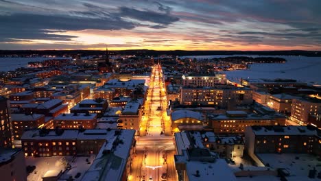 Snow-covered-cityscape-at-dusk-with-illuminated-streets,-aerial-view