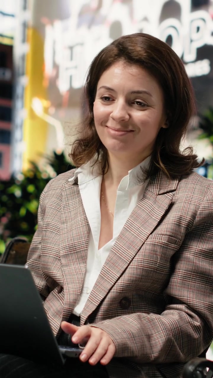 Vídeo vertical: Empresária trabalha no laptop sentada em um banco de madeira no centro da cidade.