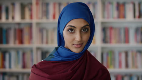 retrato joven musulmana independiente gira la cabeza sonriendo tranquila disfrutando de un éxito educativo logro usando hijab en la biblioteca estantería fondo cámara lenta