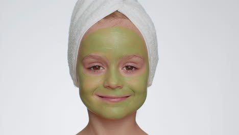 Hermosa-Niña-Sonriente-Con-Una-Toalla-En-La-Cabeza-Aplicando-Una-Mascarilla-Verde-Hidratante-Limpiadora-En-La-Cara