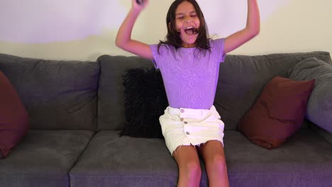 una niña hispana jugando videojuegos en línea en el sofá.