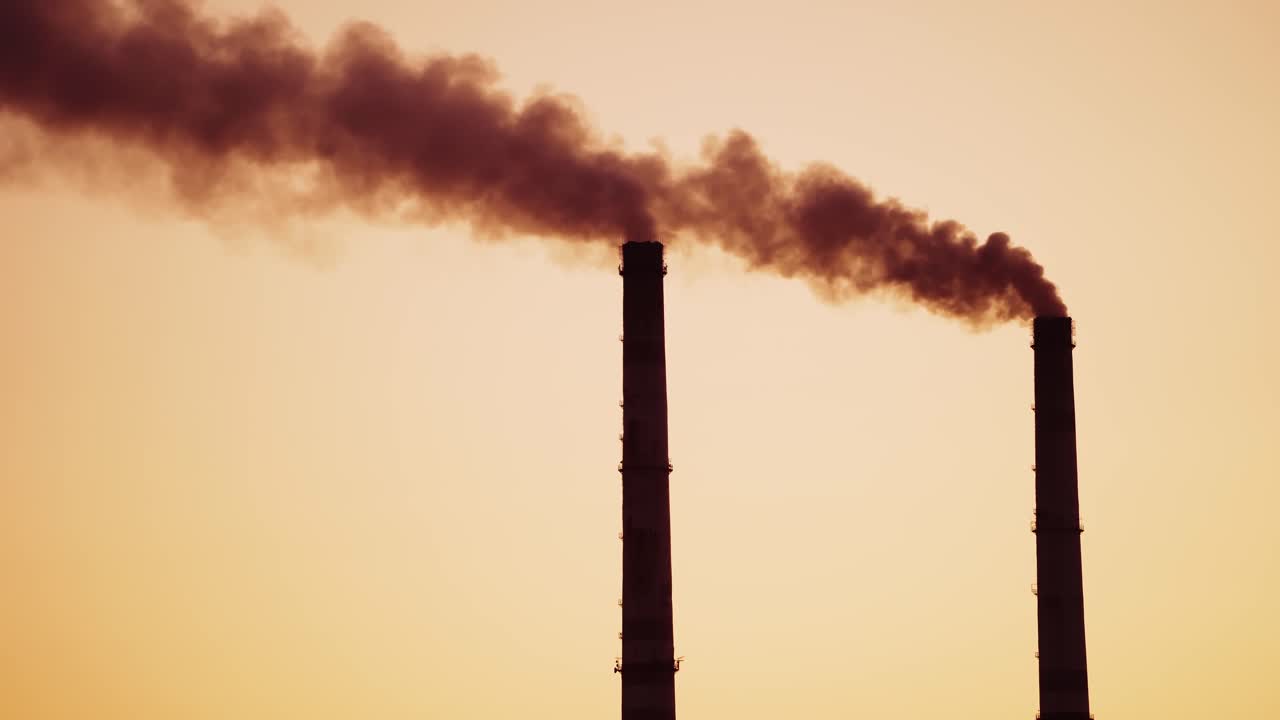 Industrial pipes with dark smoke at sunset. Dirty chemical smoke coming out from two pipes in the evening. Air pollution. Close-up.