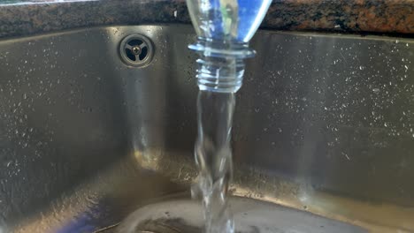 Slow-motion-shot-of-pouring-circling-water-out-of-bottle-into-sink,close-up