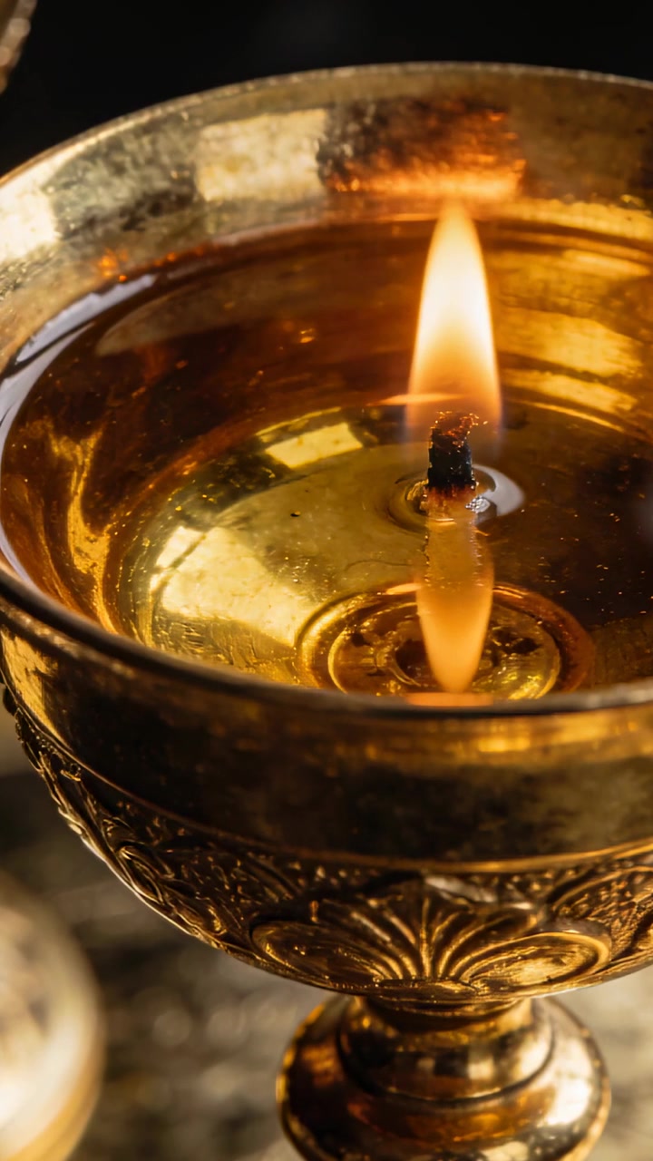 Vertical video: Flickering charred wick burning in brass oil lamp, casting oil reflection on altar