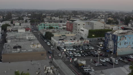 AERIAL:-Over-Venice-Beach-Boardwalk-with-Visitors-and-Palm-Trees,-Sunset,-Los-Angeles,-California