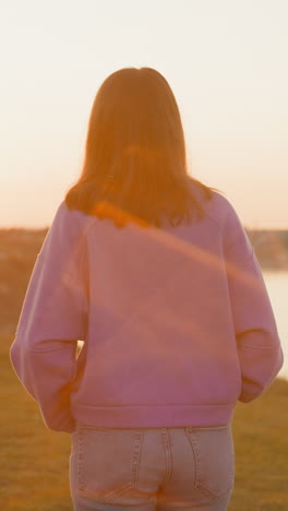 woman rests walking at sunset riverside. relaxed slim lady spends tranquil evening on hilly bank of large river at spring dusk. rural site travel