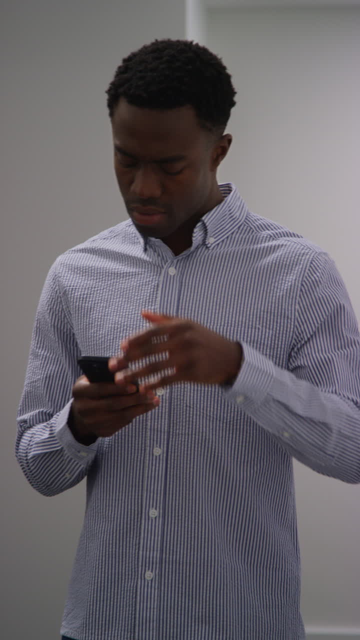 Vertical Video Of Young Businessman In Office Looking At Message With Bad News On Mobile Phone And Leaning Against Wall Looking Unhappy And Depressed