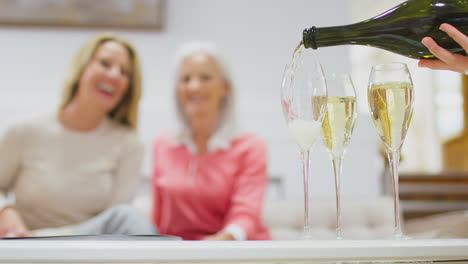 close up of champagne or prosecco being poured into glasses with two women in background