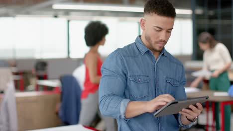 Portrait-of-biracial-man-using-a-digital-tablet-and-smiling-at-office