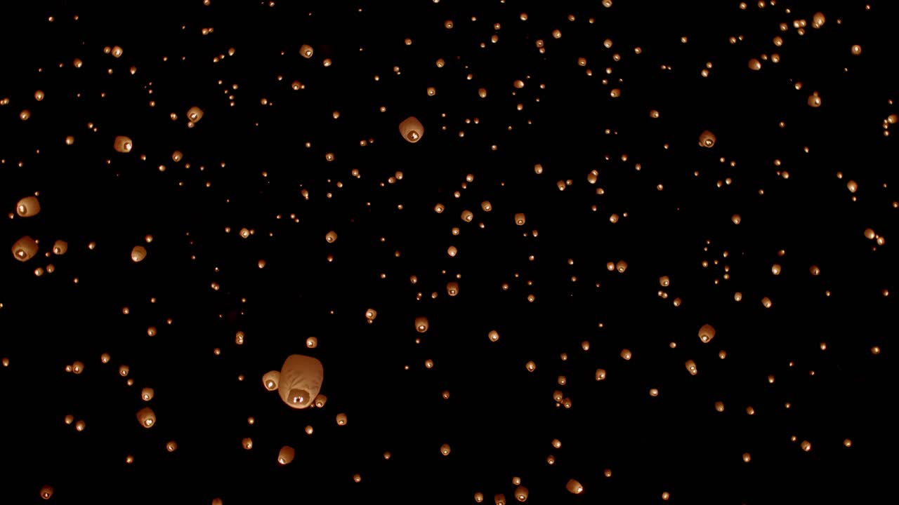 Night sky filled with paper lanterns floating away at festival in slow motion