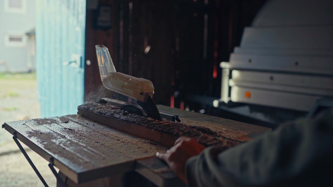 A Person is Using a Table Saw to Cut a Piece of Wood on a Workbench Indoors - Close Up