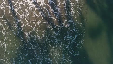 drone hovering above waves hitting the sandy beach with a pull away