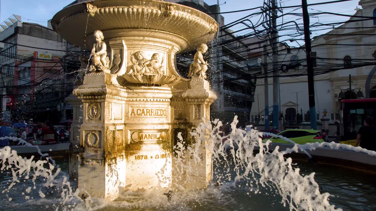 Statisk mellemshot af en historisk stenfontæne med kerubstatuer og plaskende vand.