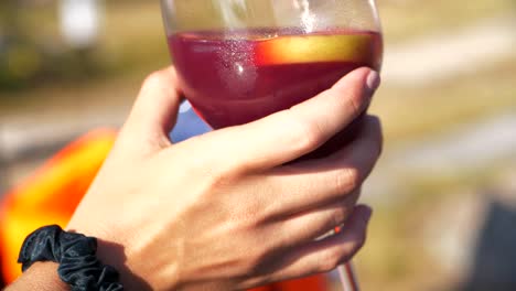 mano femenina con toque sensual sosteniendo un vaso de sangría fresca, ambiente de verano