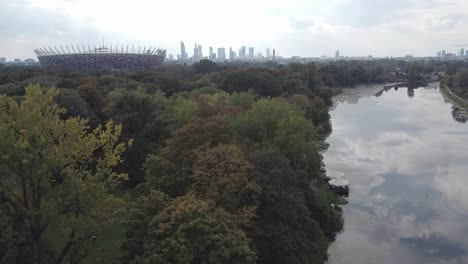 Beautiful-drone-revealing-shot-of-warsaw-national-stadium-of-poland,-city-and-lake-in-the-background