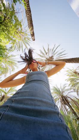 playful woman in denim dress with flying hair under palm trees