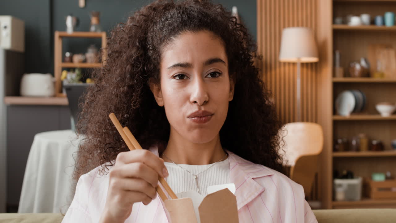 Woman eating take-out food with chopsticks at home