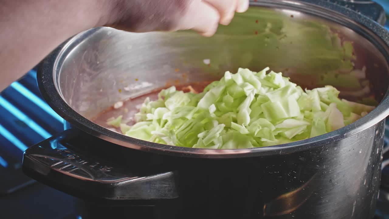 양배추를 강철 냄비에 수프에 붓고 나무 숟가락으로 휘젓고 닫습니다.