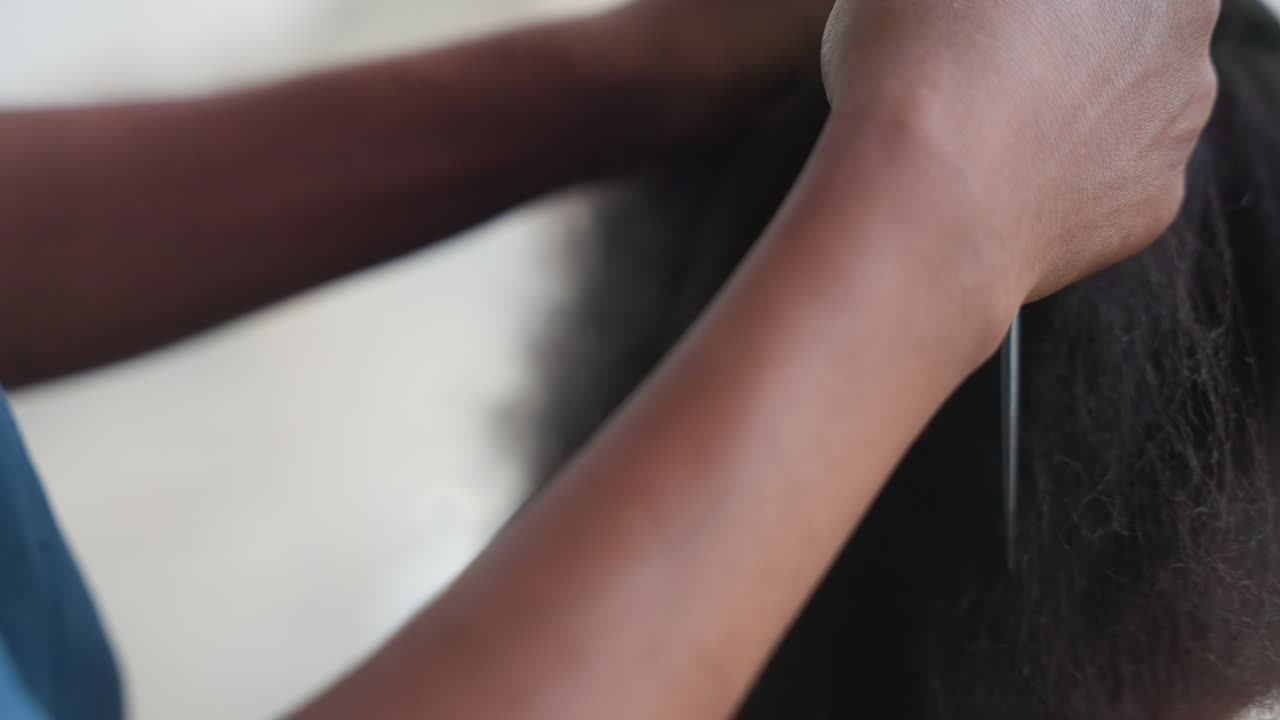 Nærbillede af omsorgsperson, der udreder et barns hår med kam og fingerspidser, intim rolig atmosfære, tekstureret afrohår, omhyggeligt hovedbundsarbejde, tålmodig plejerutine, beskyttende stylingritual, hjemlige omgivelser