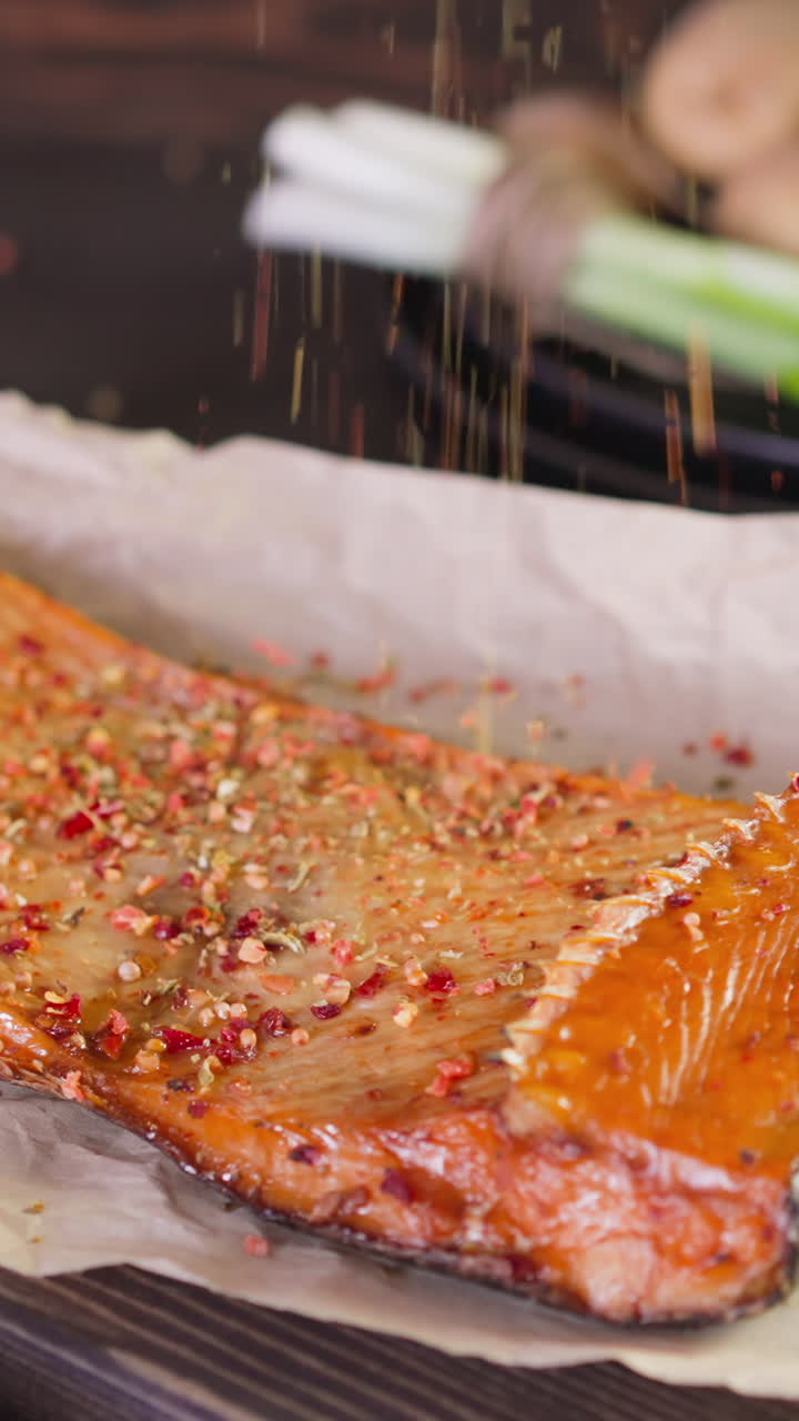 Pouring spices onto expensive smoked trout piece with spices lying on crumpled parchment served on wooden board close view slow motion