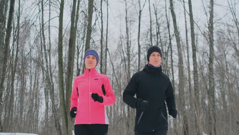 Un-Hombre-Y-Una-Mujer-Con-Una-Chaqueta-Rosa-En-Invierno-Corriendo-Por-El-Parque-En-Cámara-Lenta.-Estilo-De-Vida-Saludable