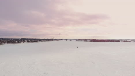 SLOW-MOTION:-A-male-athlete-is-engaged-in-kiting-on-skis.-He-rolls-on-the-ice-of-a-large-lake.-Rolling,-he-performs-various-jumps,-coups-and-other-exercises.-Windy-sunny-winter-day