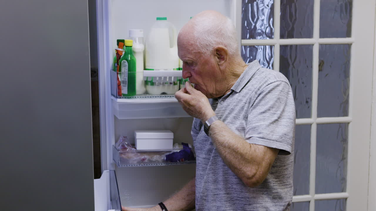 Elderly man looks in the refrigerator