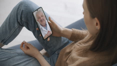 woman checks possible symptoms with professional physician using online video chat. young girl sick at home using smartphone to talk to her doctor via video conference medical app.