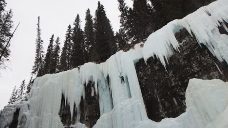 wide shot of woman ice climbing on frozen water fall