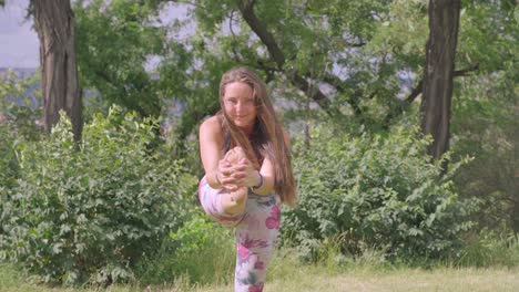 Static-footage-of-young-woman,-performing-standing-head-to-knee-yoga-pose-outdoors