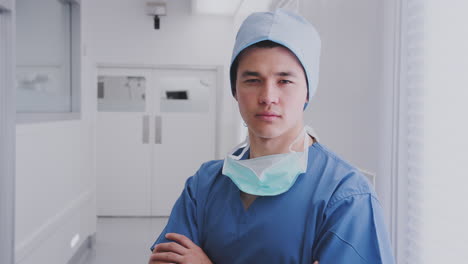 Portrait-Of-Male-Surgeon-Wearing-Scrubs-And-Mask-Standing-In-Hospital-Corridor