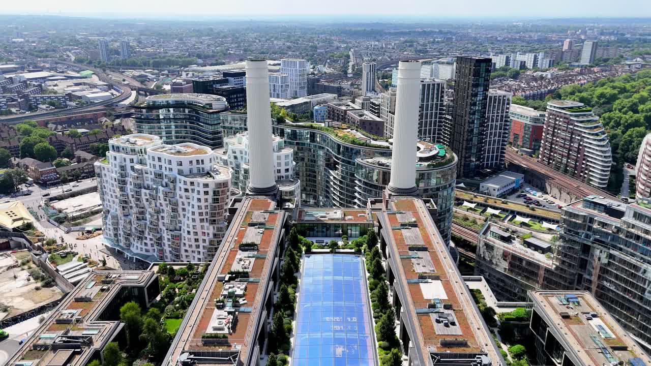 Dynamic drone fly-through between Battersea Power Station’s iconic chimneys in London, showcasing industrial design, rooftop gardens, skyline views, and the ever developing area