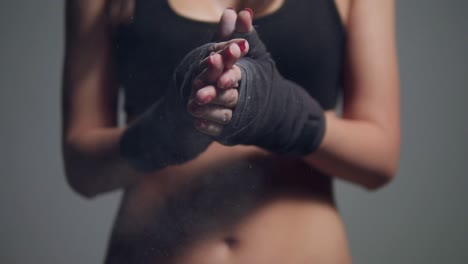 close up view of young beautiful fit woman dusting powder on her hands wrapped in boxing tapes as she prepares for a workout at