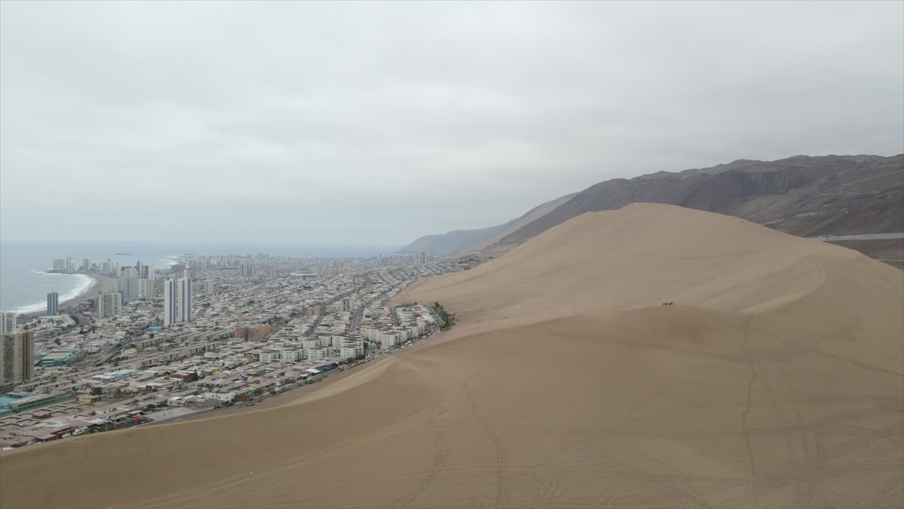 toma aérea de un avión no tripulado de la duna en primer plano y la ciudad moderna de iquique en el fondo