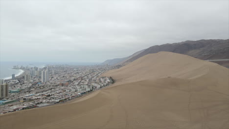 aerial drone shot of dune on foreground and modern town of iquique on the background