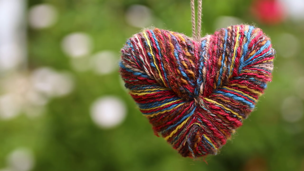 Colorful Yarn Heart Hanging Outdoors Handcrafted Multicolor Yarn Heart Suspended Against Soft Green Garden