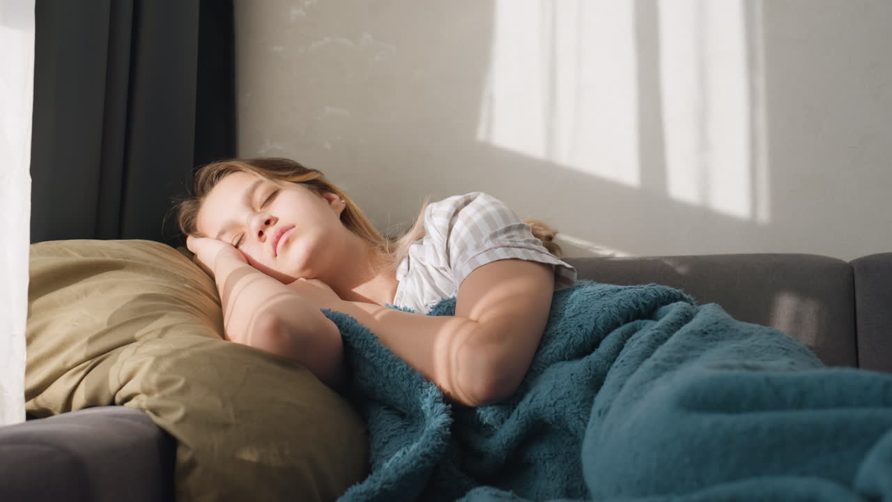 Woman Resting Under Soft Blanket, Female Relaxing On Sofa With Teal Blanket During Calm Daytime, Casual Scene Of Woman Lounging Quietly Under Blanket Amidst Tranquil Sunlight At Home