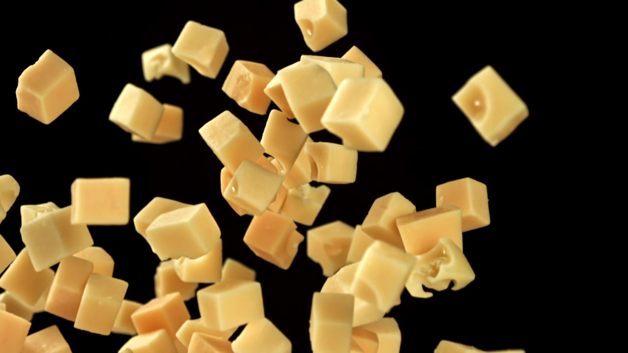 Cubes de fromage tombant et flottant au ralenti sur fond noir.