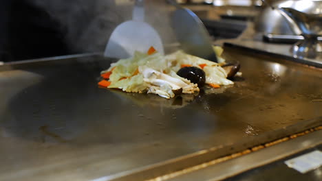 close-up of a skilled chef preparing teppanyaki japanese cuisine on a hot iron griddle in front of guests, grilling fresh ingredients with flair. perfect for japanese food culture and live cooking